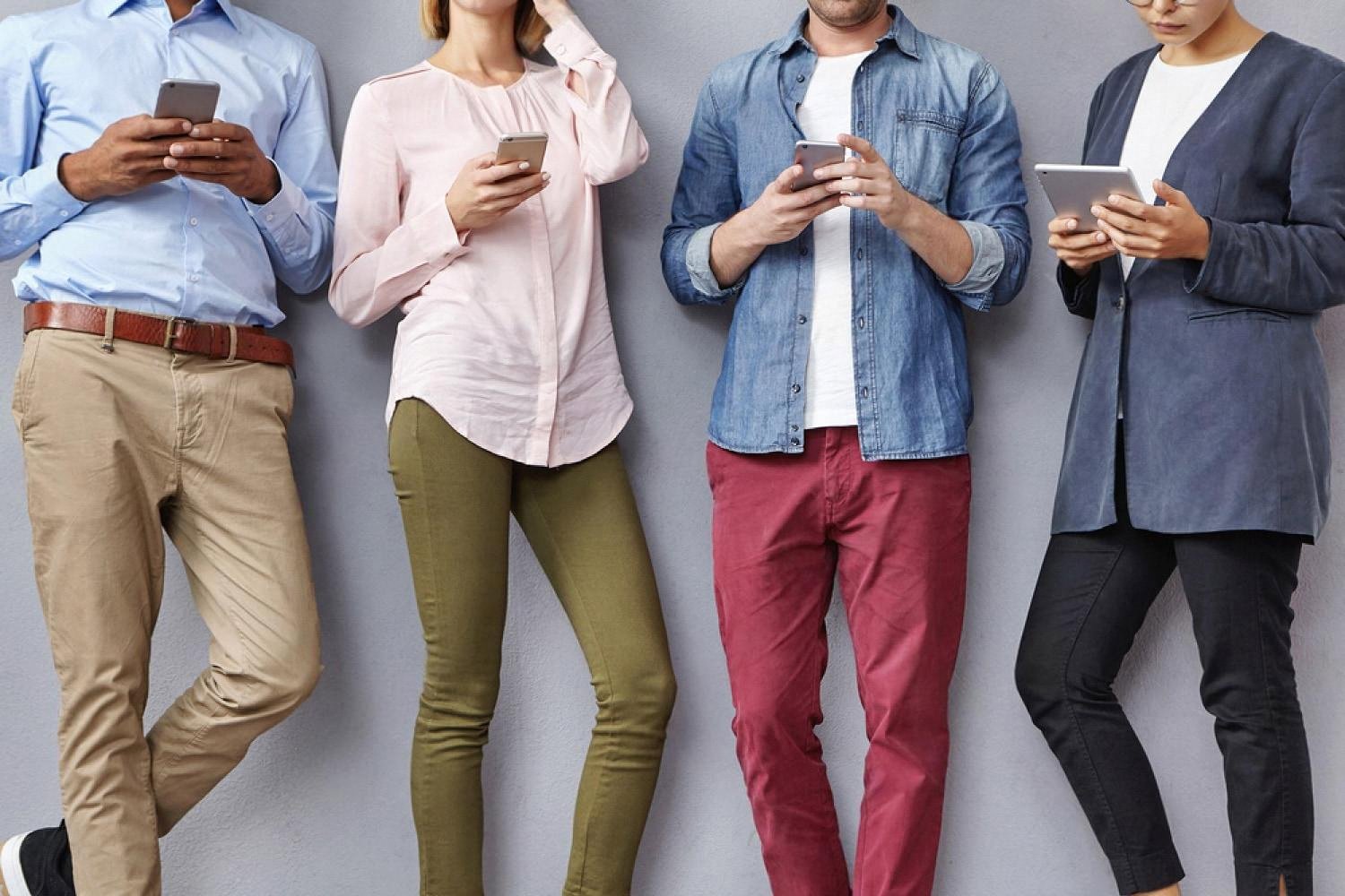 Four visitors checking their phones while waiting for their turn to be called at a service center